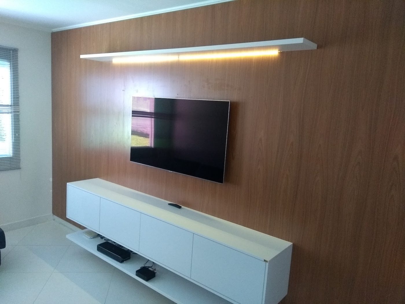 Painel de TV planejado em madeira com rack suspenso e nicho iluminado